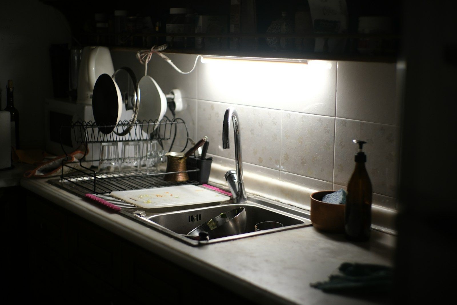 Dishes in a drying rack beside a kitchen sink under a task light.